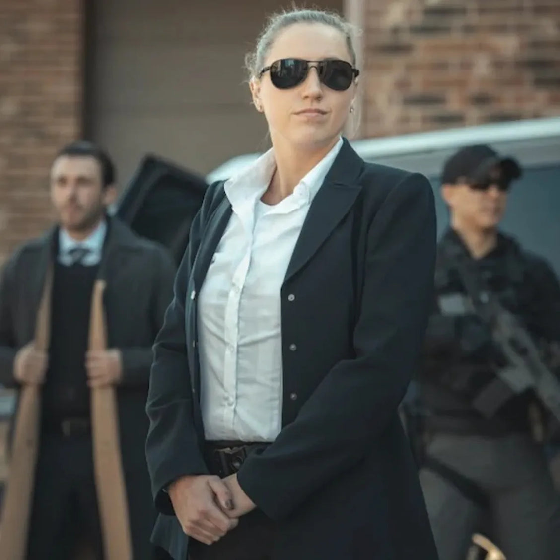 Mujer agente de proteccion VIP vestida con traje sastre negro y lentes oscuros, utilizando la playera blindada discreta para dama Miguel Caballero en un entorno corporativo de custodia elite.